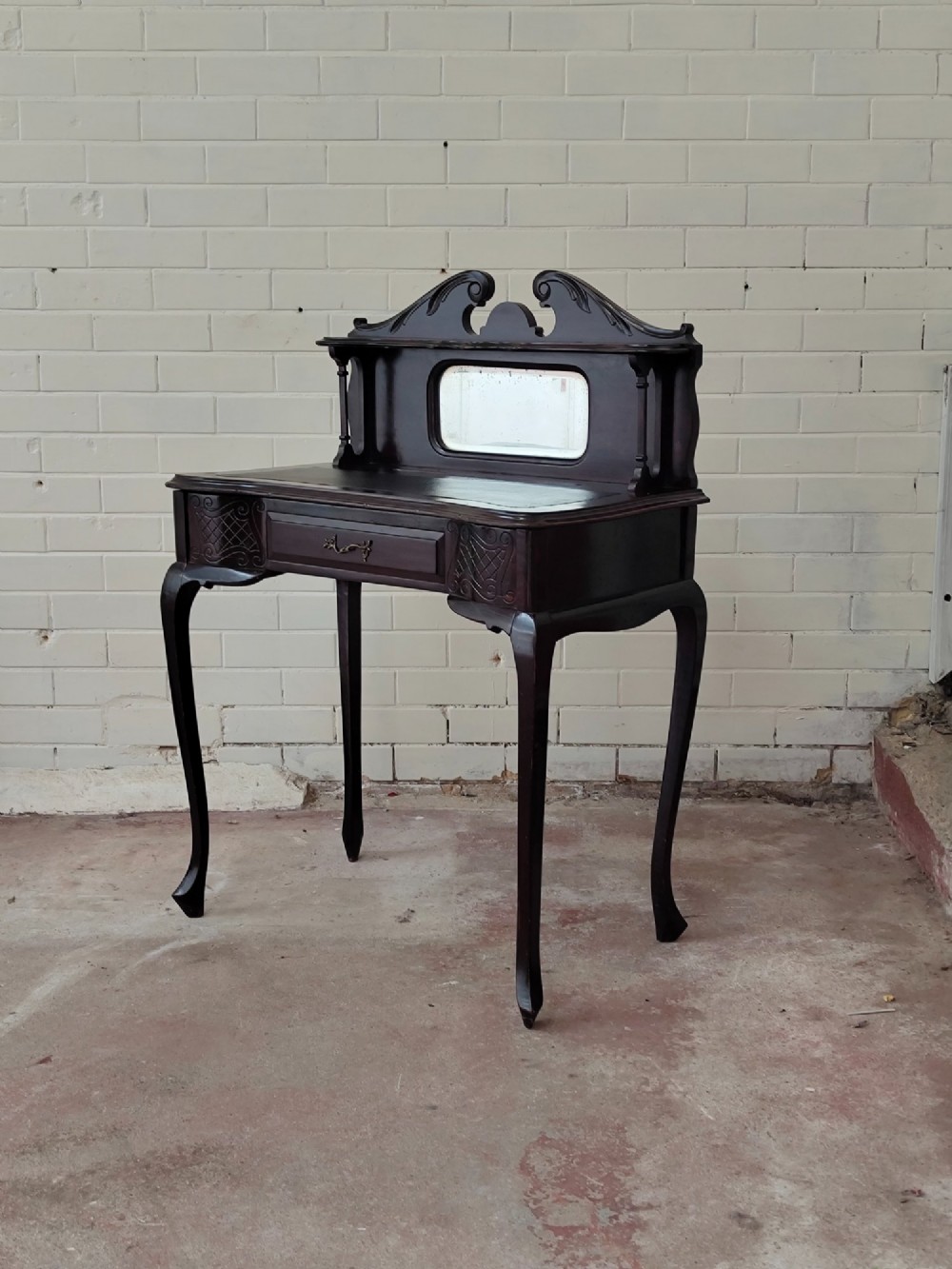 A dark mahogany Victorian ladies writing desk featuring slender cabriole legs, a single drawer, carved lattice details, and a raised back structure with a small central mirror. View X