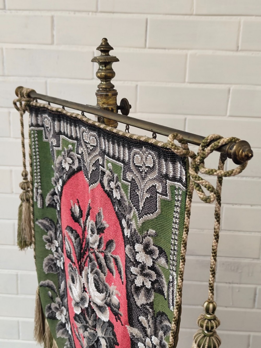 An antique Victorian brass pole screen featuring a green embroidered floral tapestry banner, fringed border, tassels, and a dark green velvet base. View XII