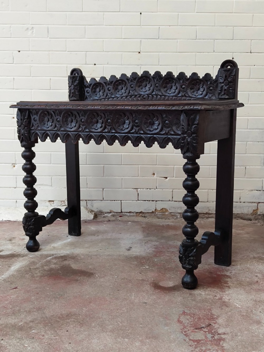 Dark carved oak hall table featuring a carved floral gallery, relief apron, bobbin-turned front legs, and lower stretcher.