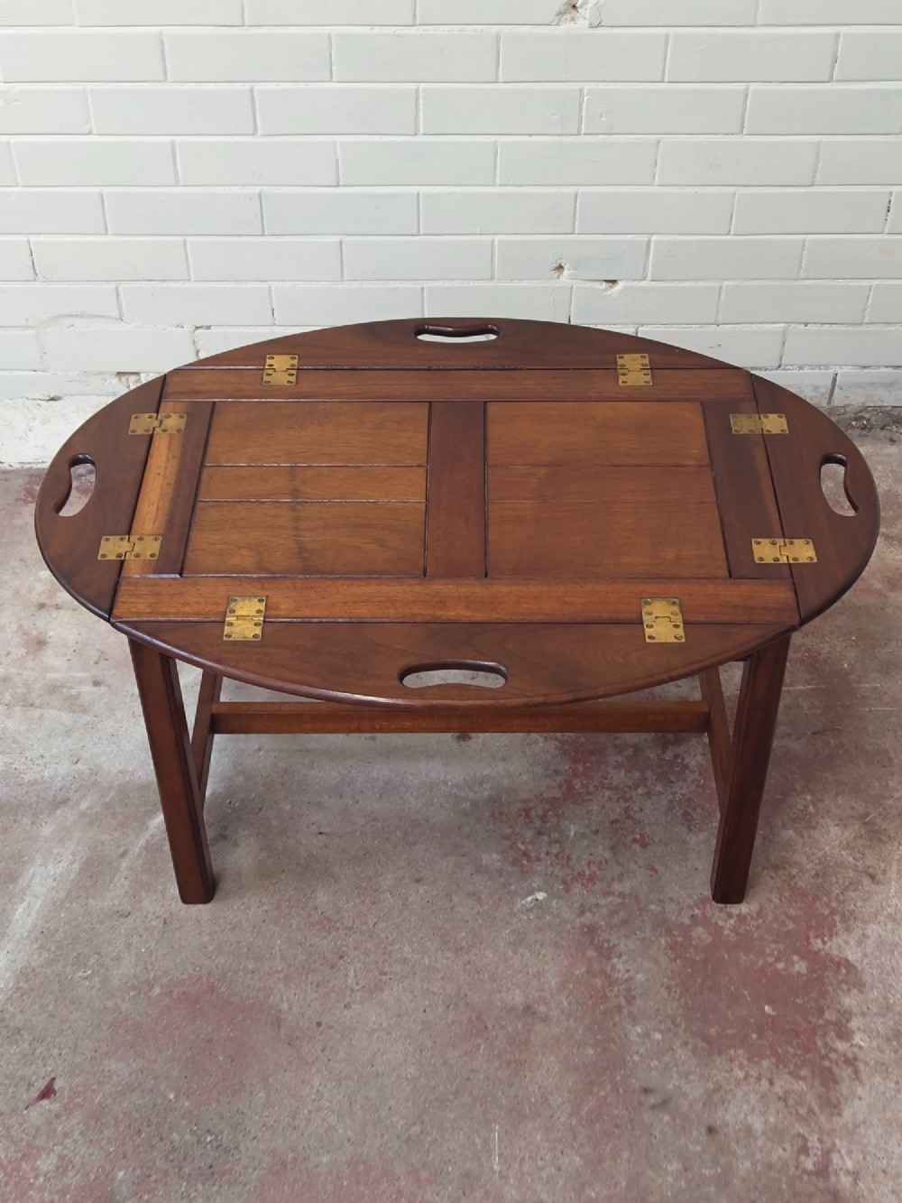An antique mahogany butlers tray with hinged folding sides and brass fittings resting on a rectangular wooden stand. View IV