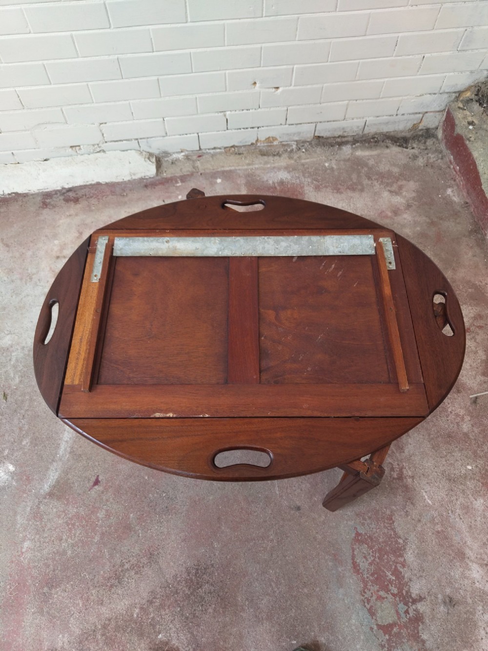 An antique mahogany butlers tray with hinged folding sides and brass fittings resting on a rectangular wooden stand. View VII
