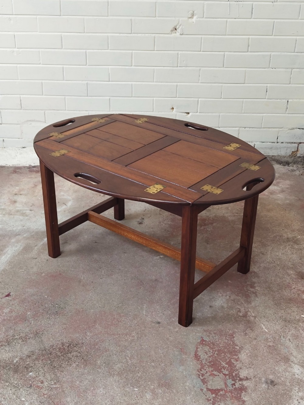An antique mahogany butlers tray with hinged folding sides and brass fittings resting on a rectangular wooden stand. View VIII