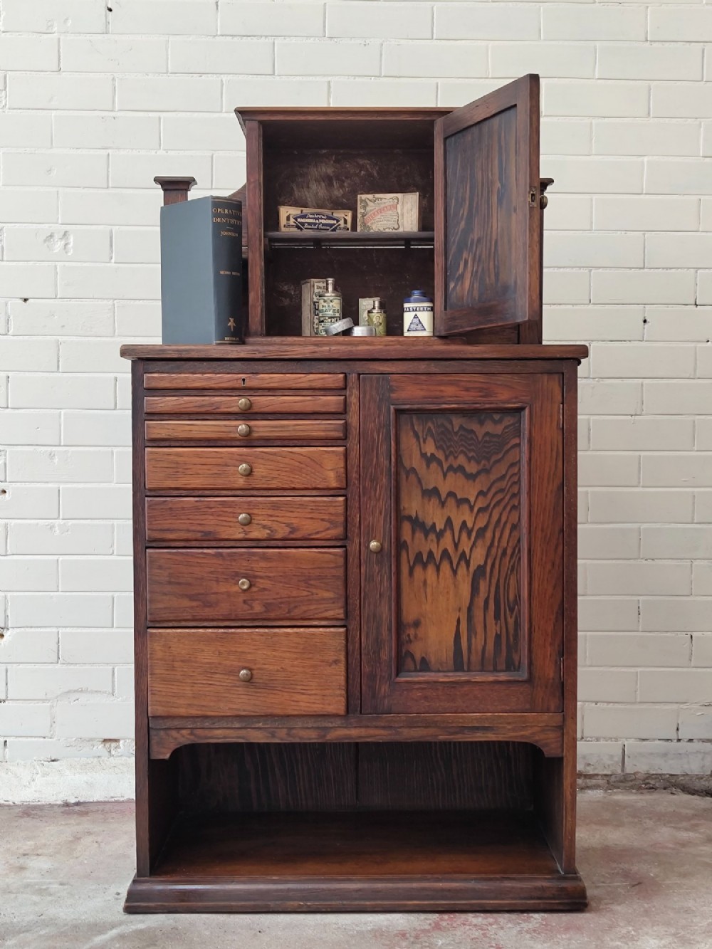 An Edwardian solid oak dentist cabinet featuring multiple shallow drawers, paneled cupboard doors, brass turned knobs, and an open lower shelf. View II