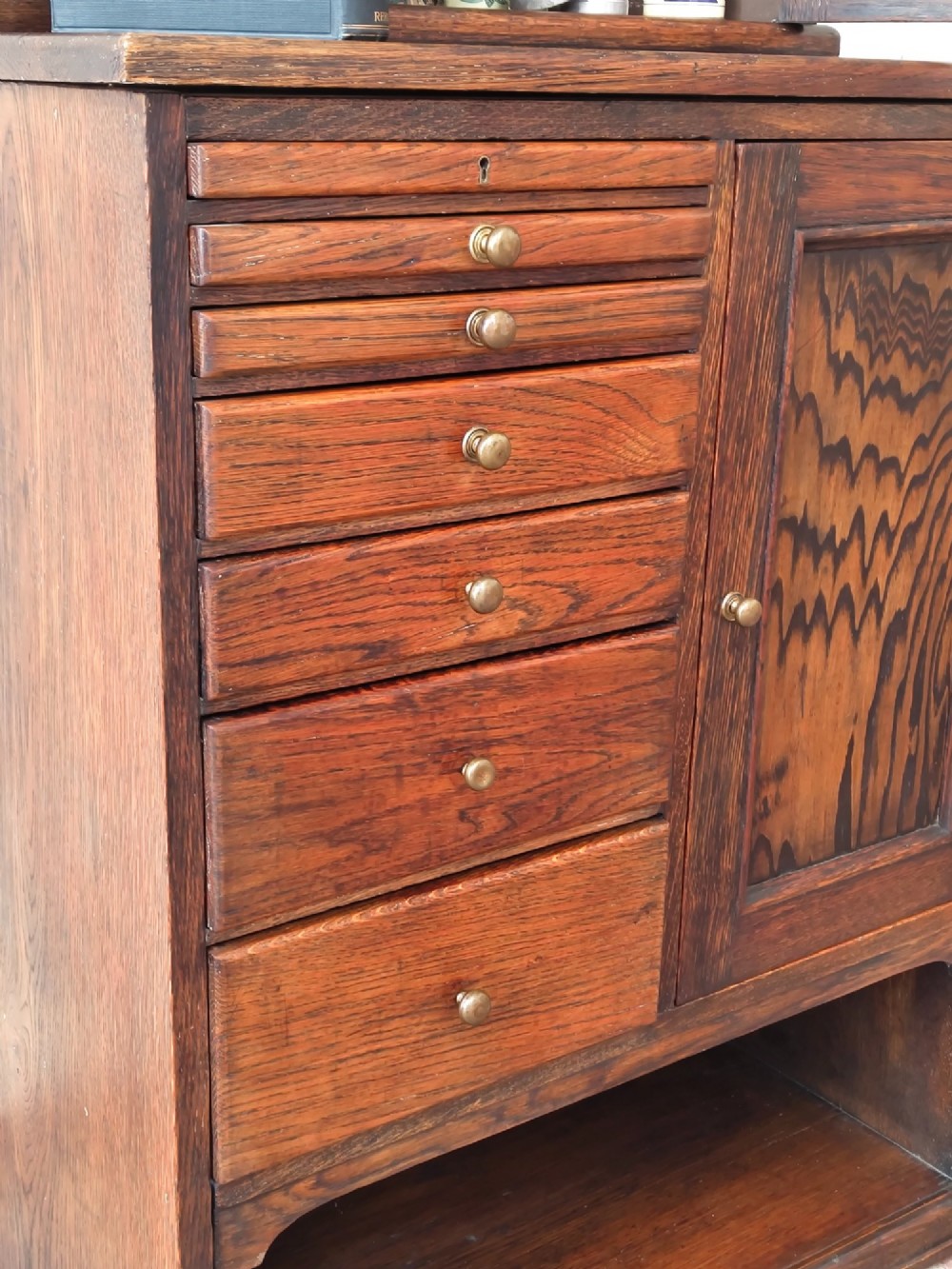 An Edwardian solid oak dentist cabinet featuring multiple shallow drawers, paneled cupboard doors, brass turned knobs, and an open lower shelf. View III