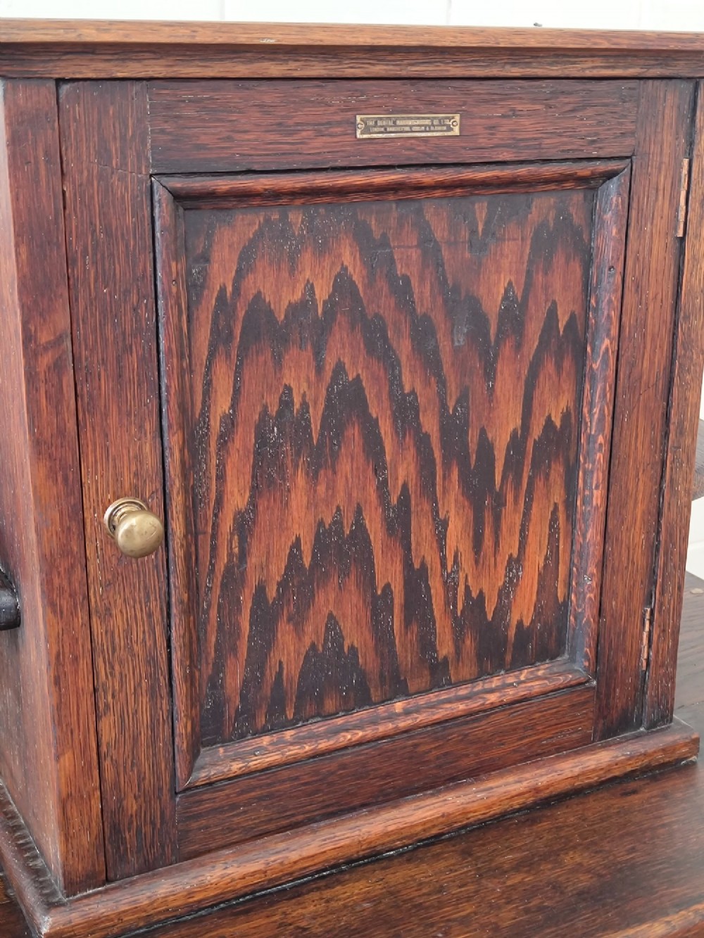 An Edwardian solid oak dentist cabinet featuring multiple shallow drawers, paneled cupboard doors, brass turned knobs, and an open lower shelf. View IV