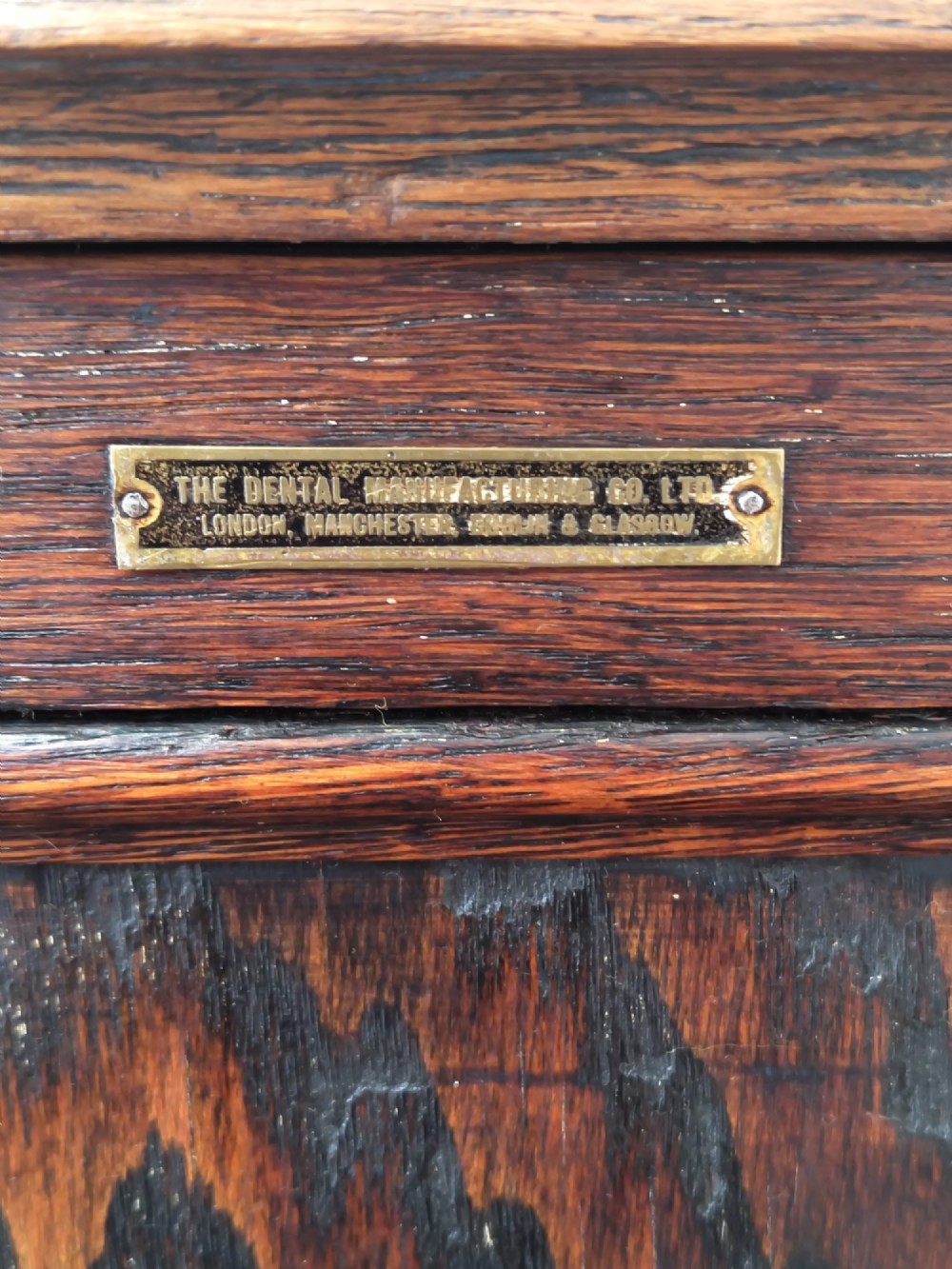 An Edwardian solid oak dentist cabinet featuring multiple shallow drawers, paneled cupboard doors, brass turned knobs, and an open lower shelf. View V