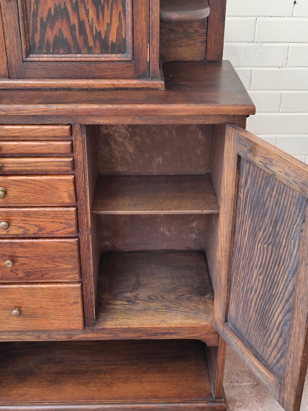 An Edwardian solid oak dentist cabinet featuring multiple shallow drawers, paneled cupboard doors, brass turned knobs, and an open lower shelf. View VI