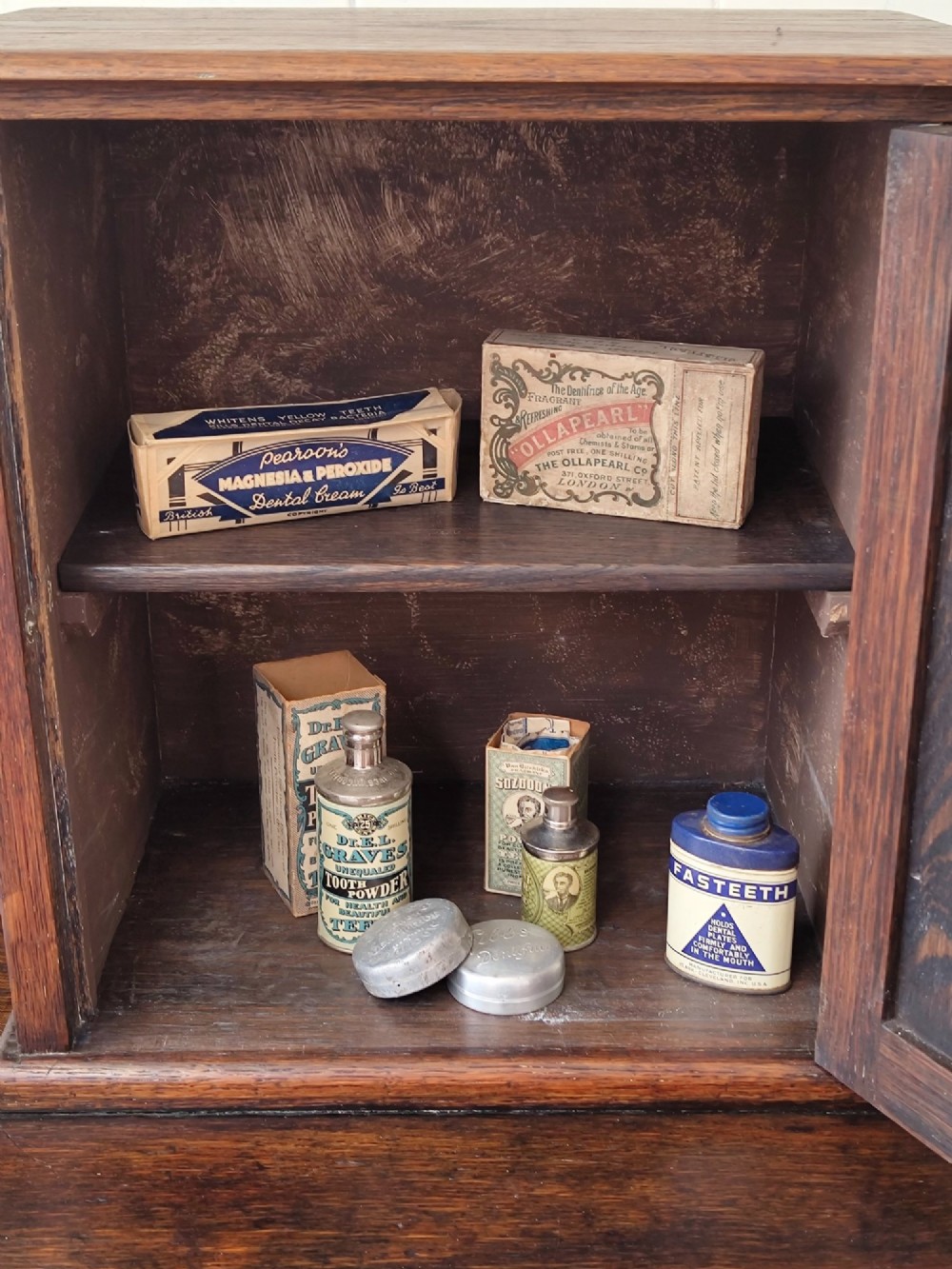 An Edwardian solid oak dentist cabinet featuring multiple shallow drawers, paneled cupboard doors, brass turned knobs, and an open lower shelf. View VII