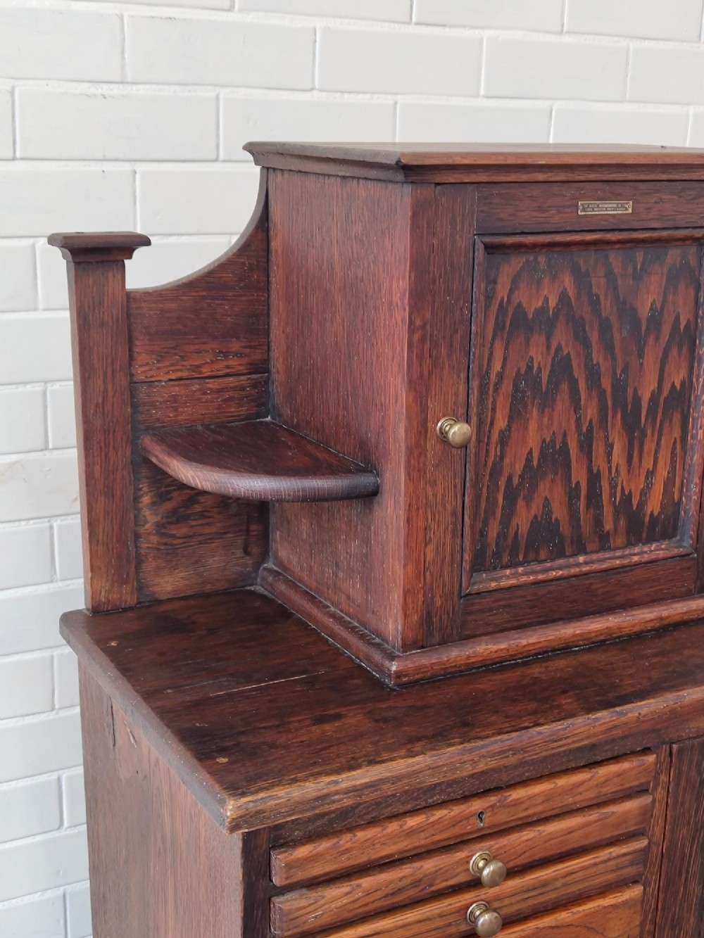 An Edwardian solid oak dentist cabinet featuring multiple shallow drawers, paneled cupboard doors, brass turned knobs, and an open lower shelf. View XII