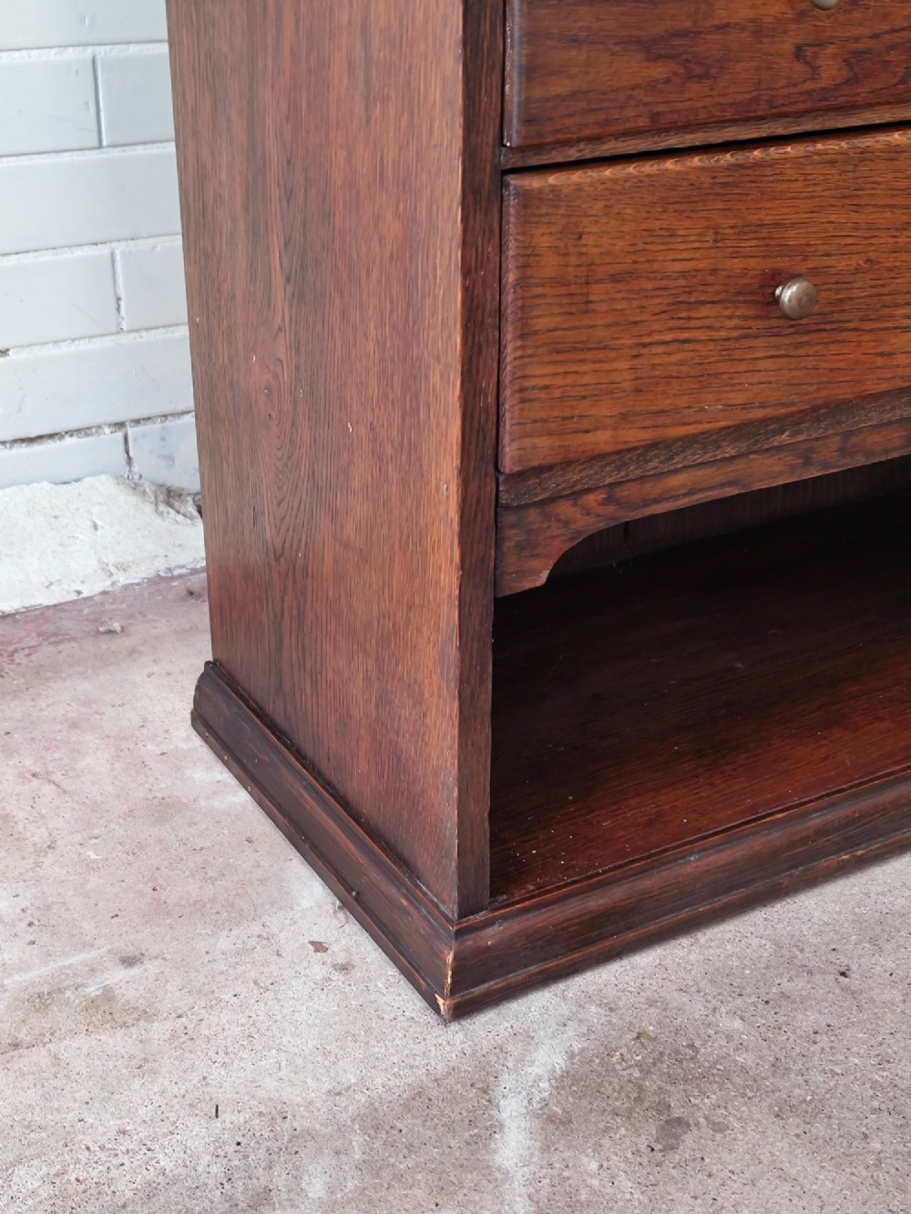 An Edwardian solid oak dentist cabinet featuring multiple shallow drawers, paneled cupboard doors, brass turned knobs, and an open lower shelf. View XIV
