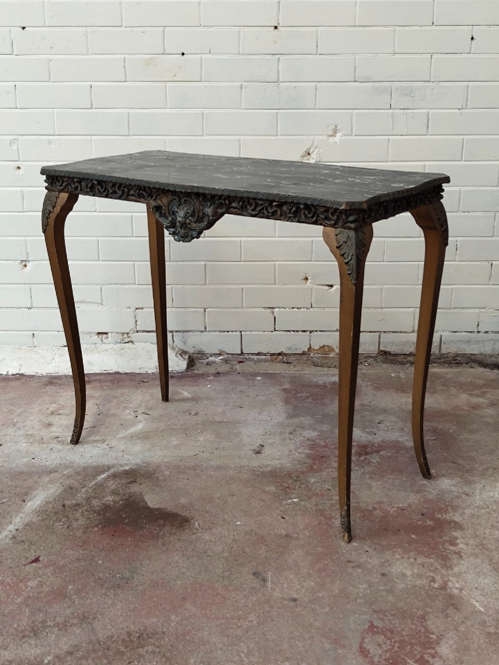A diminutive French Rococo style console table featuring slender gilt cabriole legs, carved aprons, and a dark faux marble top. View II