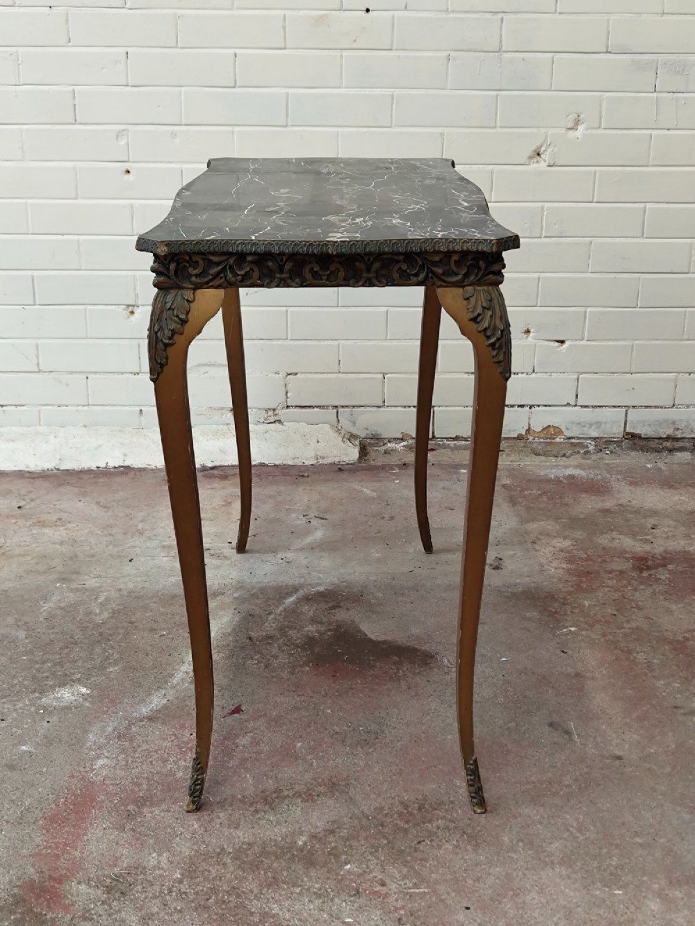 A diminutive French Rococo style console table featuring slender gilt cabriole legs, carved aprons, and a dark faux marble top. View IV