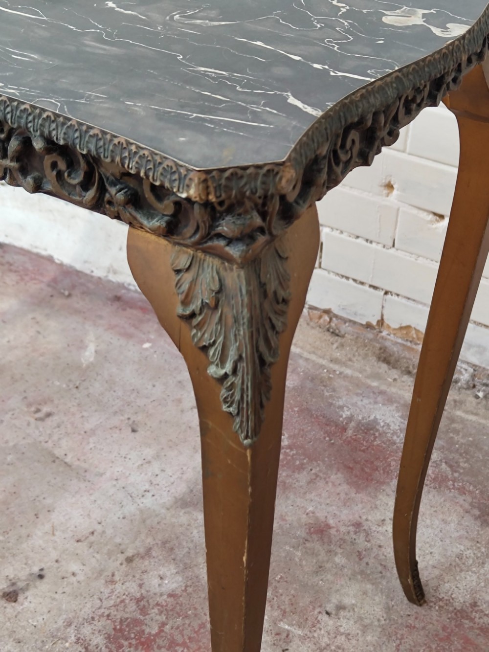 A diminutive French Rococo style console table featuring slender gilt cabriole legs, carved aprons, and a dark faux marble top. View X