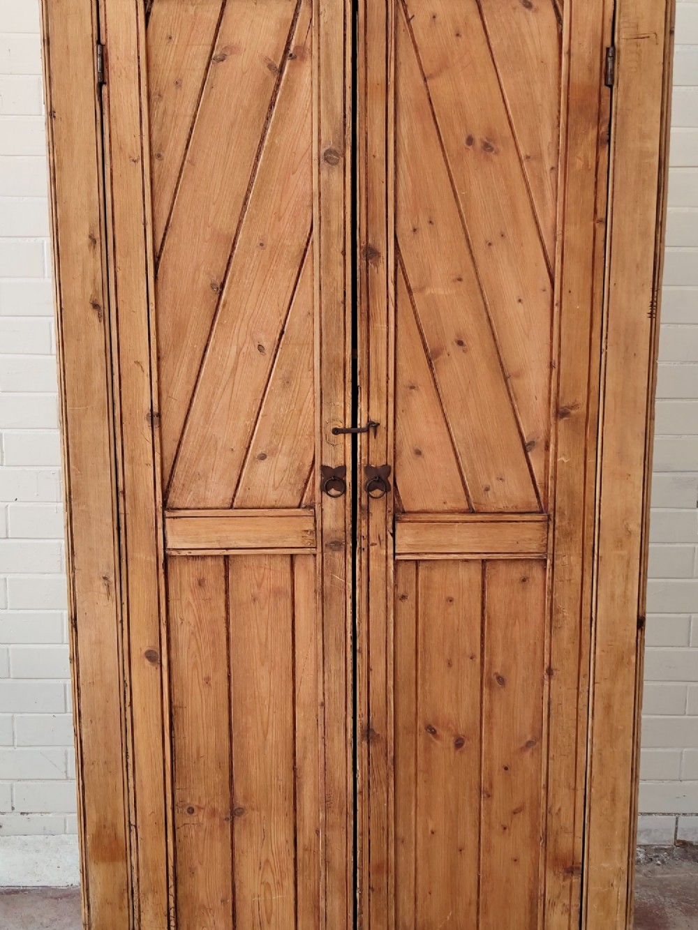 A tall antique pitch pine corner wardrobe featuring double doors with diagonal timber panels and a moulded top cornice. View IV