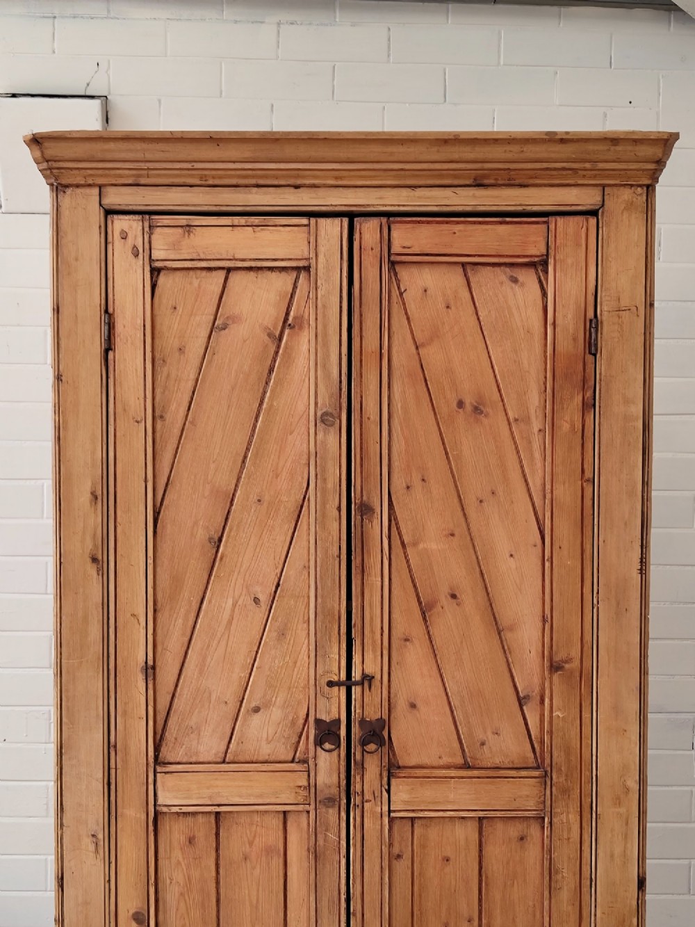 A tall antique pitch pine corner wardrobe featuring double doors with diagonal timber panels and a moulded top cornice. View V