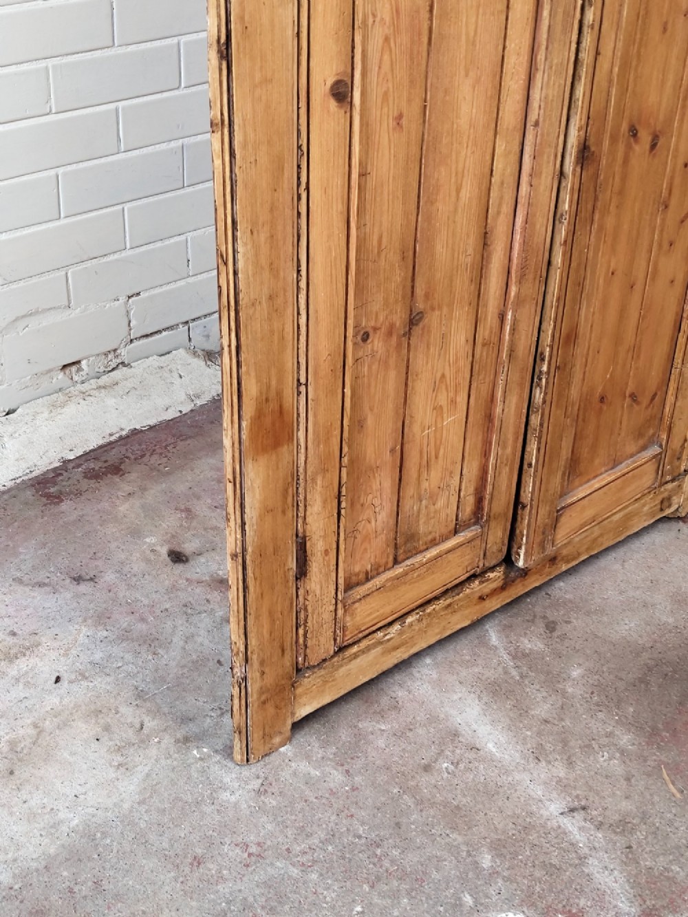 A tall antique pitch pine corner wardrobe featuring double doors with diagonal timber panels and a moulded top cornice. View VII