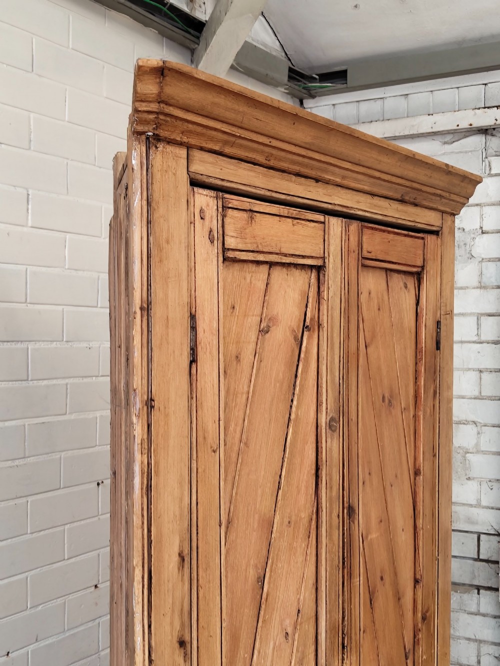 A tall antique pitch pine corner wardrobe featuring double doors with diagonal timber panels and a moulded top cornice. View VIII