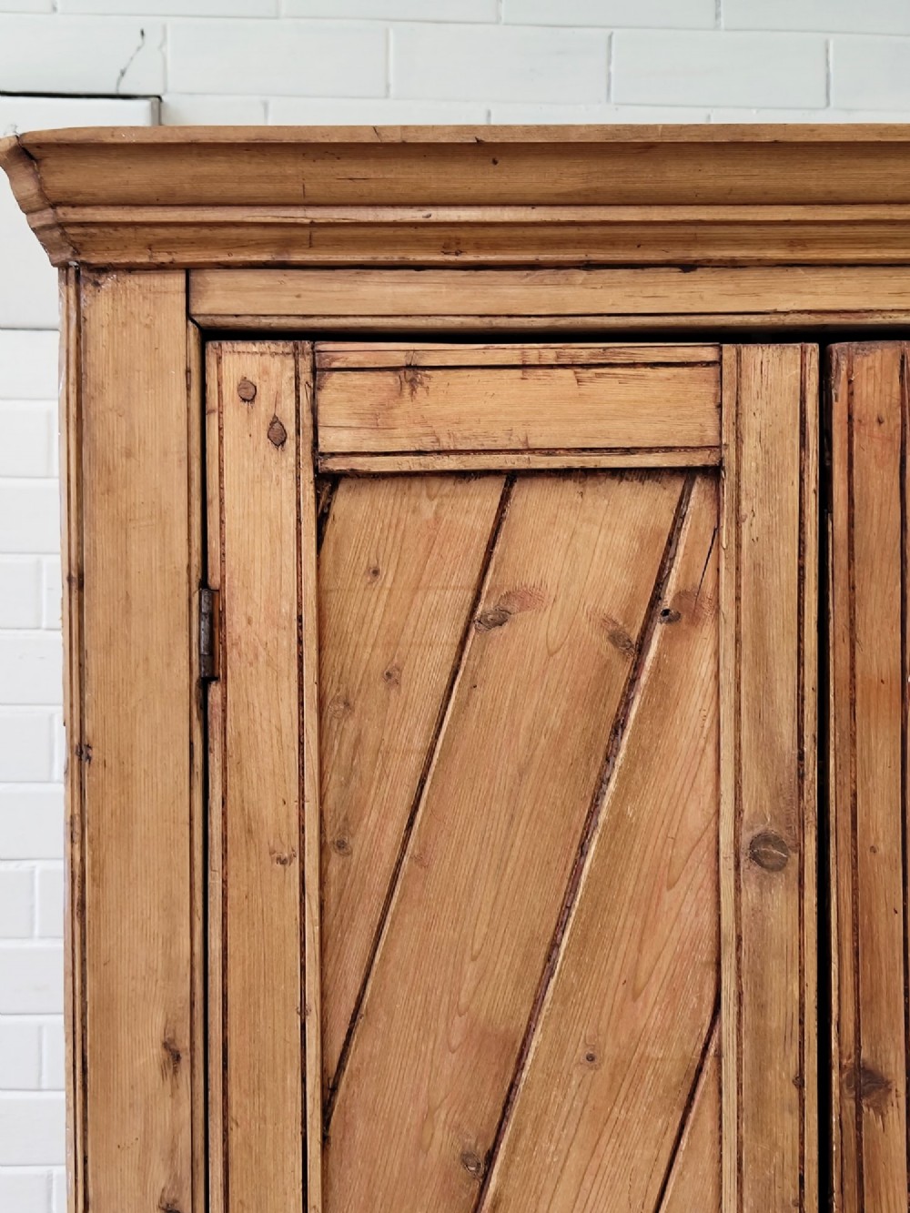 A tall antique pitch pine corner wardrobe featuring double doors with diagonal timber panels and a moulded top cornice. View XI