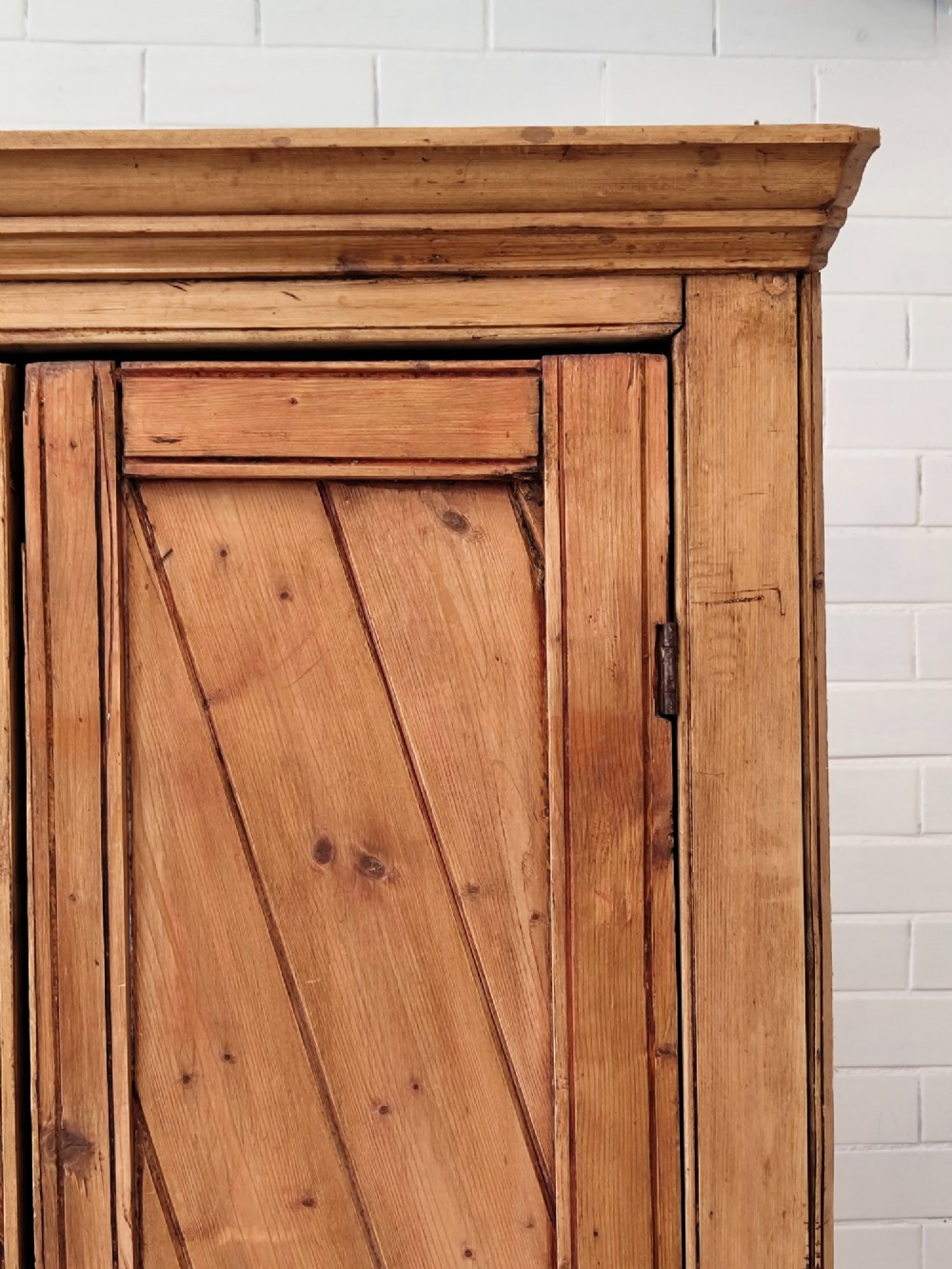 A tall antique pitch pine corner wardrobe featuring double doors with diagonal timber panels and a moulded top cornice. View XII