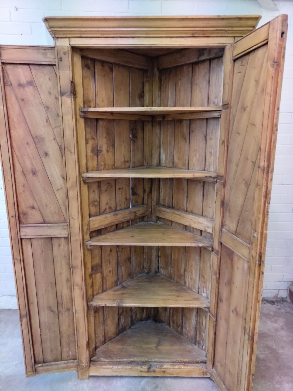A tall antique pitch pine corner wardrobe featuring double doors with diagonal timber panels and a moulded top cornice. View XIII