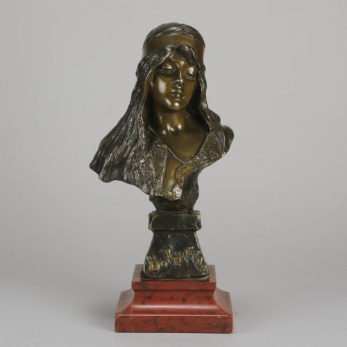 fig 1. An Art Nouveau patinated bronze bust of a young woman with long hair and a headband mounted on a red marble base.