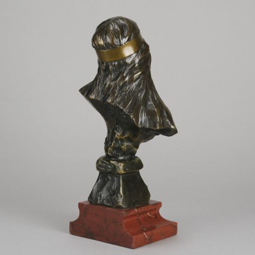 fig 3. An Art Nouveau patinated bronze bust of a young woman with long hair and a headband mounted on a red marble base.