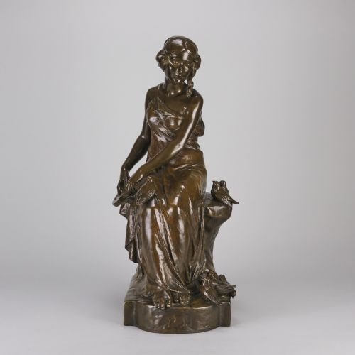 fig 1. A dark brown patinated bronze sculpture depicting a seated woman in classical draped attire interacting with small birds, set on an integral bronze base.