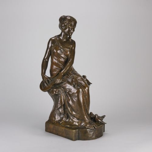 fig 3. A dark brown patinated bronze sculpture depicting a seated woman in classical draped attire interacting with small birds, set on an integral bronze base.
