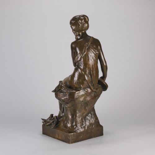 fig 4. A dark brown patinated bronze sculpture depicting a seated woman in classical draped attire interacting with small birds, set on an integral bronze base.