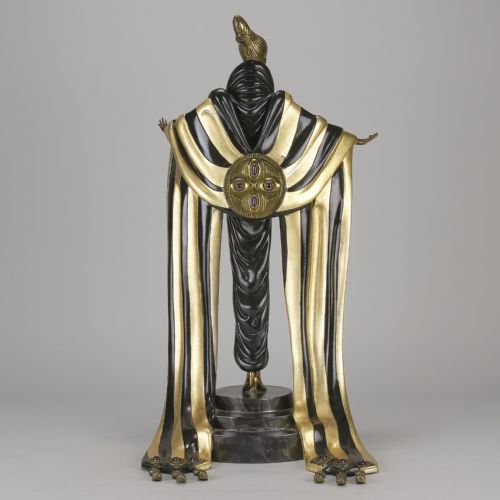 fig 1. An Art Deco cold-painted bronze figurine depicting a female figure in a floor-length black and gold robe standing on a stepped dark base.