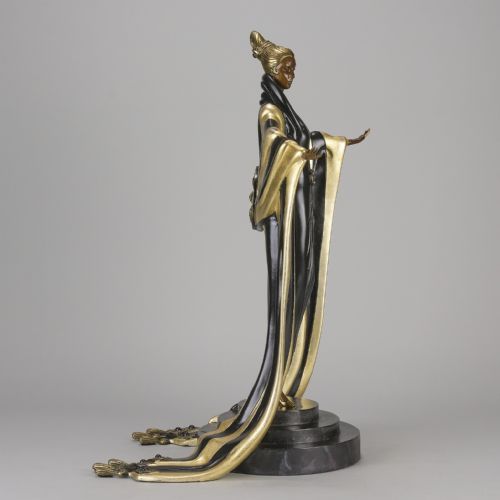 fig 4. An Art Deco cold-painted bronze figurine depicting a female figure in a floor-length black and gold robe standing on a stepped dark base.