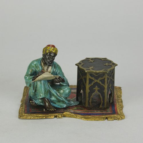 fig 1. A Viennese cold-painted bronze sculpture depicting a seated scholar in a turquoise robe writing beside an octagonal Moorish table on a patterned carpet.