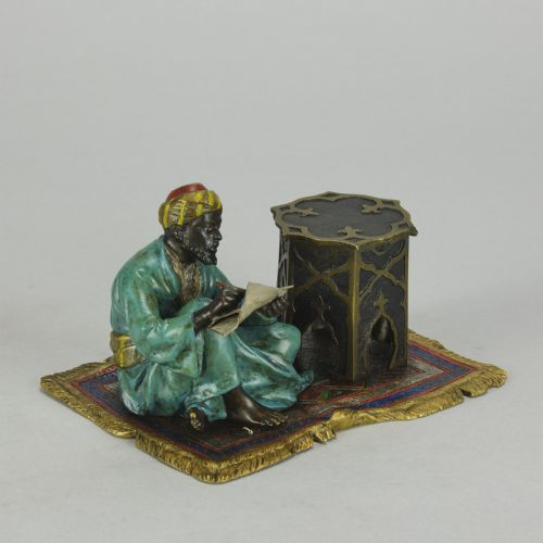 fig 2. A Viennese cold-painted bronze sculpture depicting a seated scholar in a turquoise robe writing beside an octagonal Moorish table on a patterned carpet.