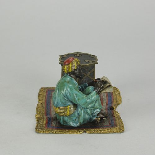 fig 3. A Viennese cold-painted bronze sculpture depicting a seated scholar in a turquoise robe writing beside an octagonal Moorish table on a patterned carpet.