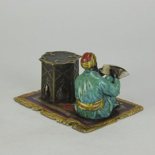 fig 4. A Viennese cold-painted bronze sculpture depicting a seated scholar in a turquoise robe writing beside an octagonal Moorish table on a patterned carpet.