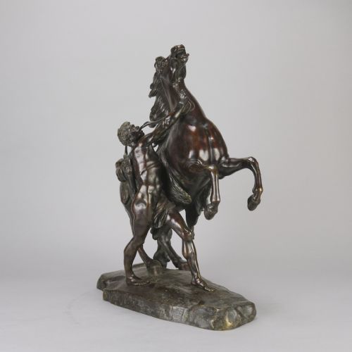 fig 2. A pair of dark brown bronze sculptures depicting rearing horses restrained by standing male figures, set on naturalistic rock bases.
