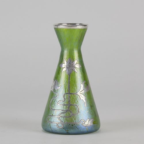 fig 1. A conical iridescent green and blue glass vase decorated with an intricate silver overlay floral design and a silver rim.