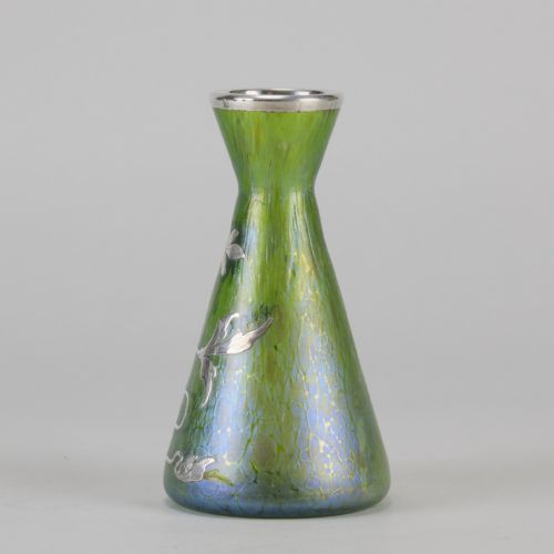 fig 7. A conical iridescent green and blue glass vase decorated with an intricate silver overlay floral design and a silver rim.