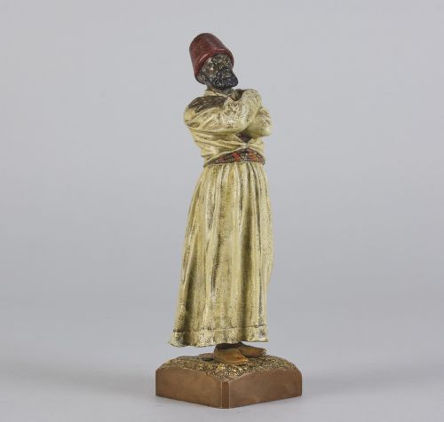 fig 1. An early twentieth-century cold-painted bronze figure depicting a bearded man in a cream robe and red fez with arms crossed on a rectangular base.