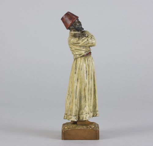 fig 2. An early twentieth-century cold-painted bronze figure depicting a bearded man in a cream robe and red fez with arms crossed on a rectangular base.
