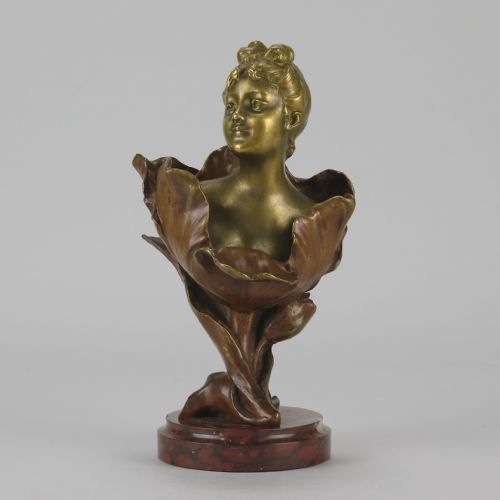 fig 1. An Art Nouveau gilt bronze bust depicting a female figure emerging from a stylised floral petal, mounted on a round reddish marble base.