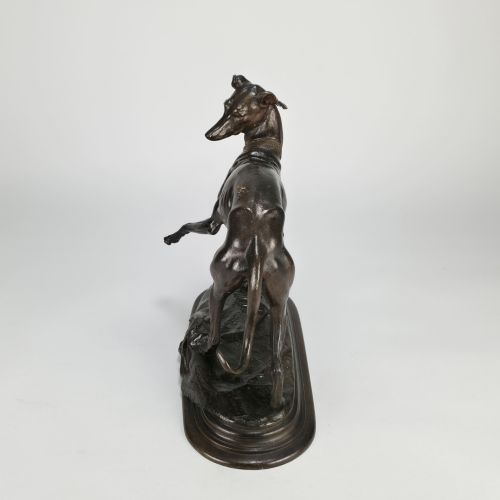 fig 6. A dark brown patinated bronze sculpture depicting a slender greyhound standing on an oval base looking back towards a fly on its hindquarters.