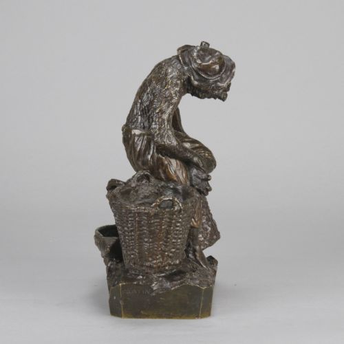 fig 1. A dark patinated bronze sculpture depicting an anthropomorphic monkey wearing trousers and a cap, standing beside two large woven baskets on a rectangular base.
