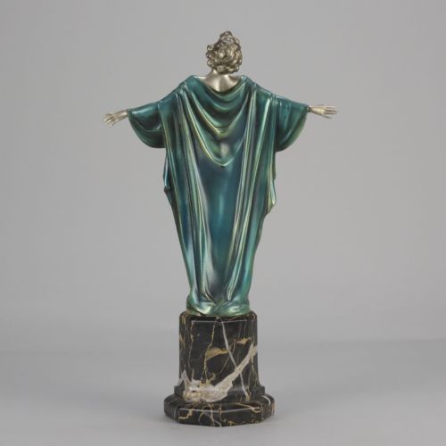 fig 1. An Art Deco cold-painted bronze sculpture depicting a silver female figure with outstretched arms wearing a teal cape, mounted on a black veined marble pedestal.