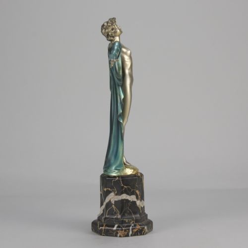 fig 6. An Art Deco cold-painted bronze sculpture depicting a silver female figure with outstretched arms wearing a teal cape, mounted on a black veined marble pedestal.