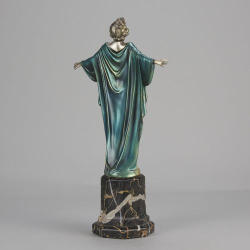 fig 7. An Art Deco cold-painted bronze sculpture depicting a silver female figure with outstretched arms wearing a teal cape, mounted on a black veined marble pedestal.