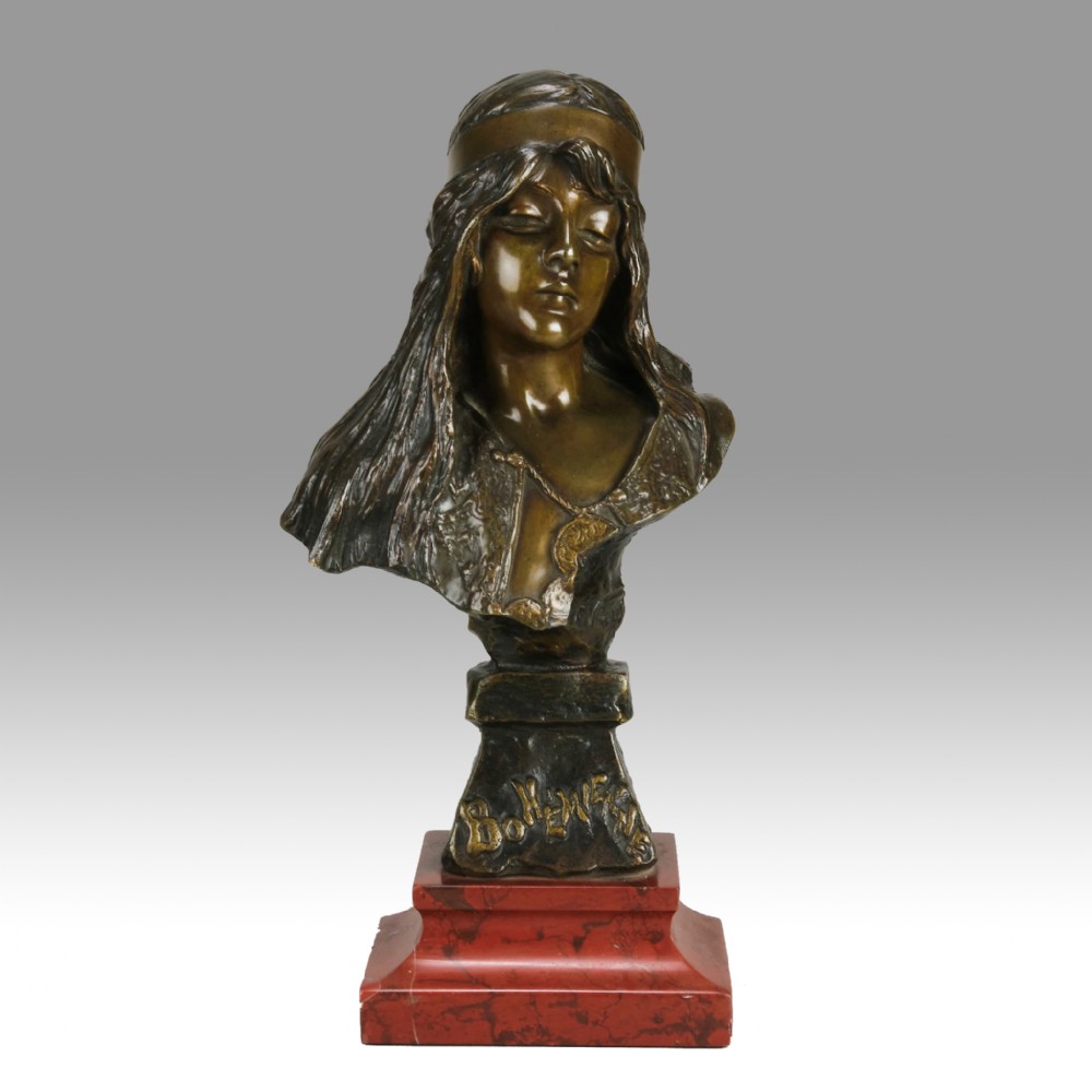 An Art Nouveau patinated bronze bust of a young woman with long hair and a headband mounted on a red marble base.
