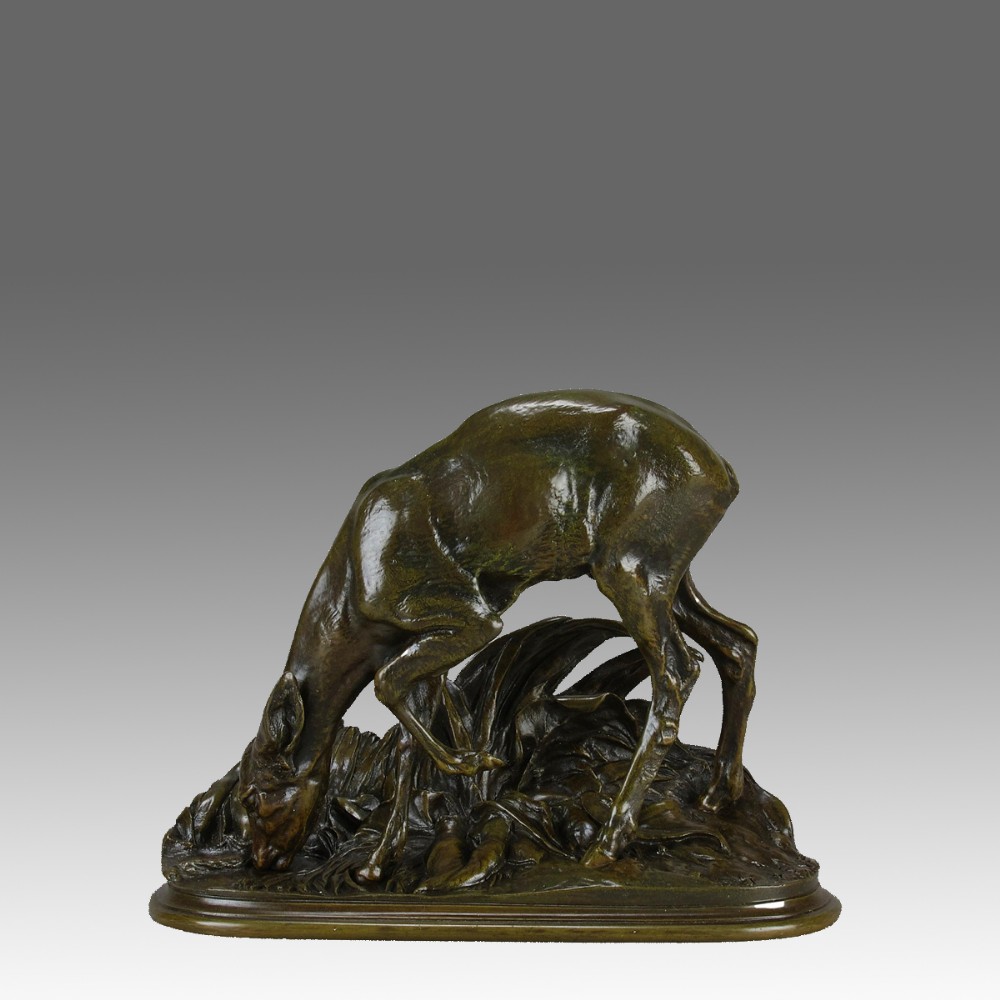 A dark patinated bronze sculpture depicting a doe bending down to drink amongst naturalistic foliage on an oval base.