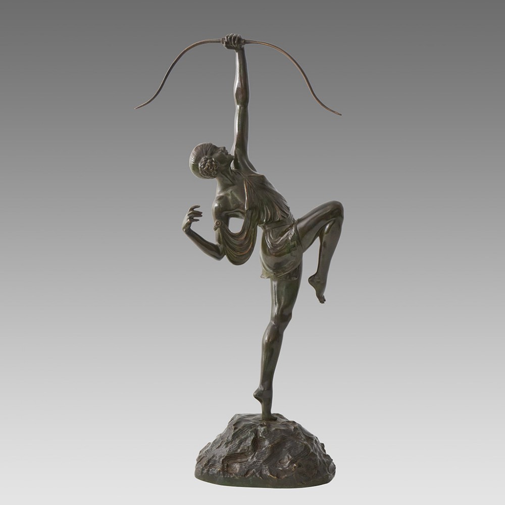 A dark patinated bronze Art Deco sculpture depicting Diana the Huntress poised dynamically on a rocky base with a bow held overhead.