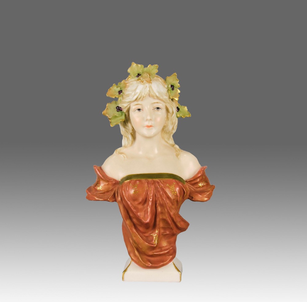 A late nineteenth-century Art Nouveau ceramic bust depicting a blonde maiden with leaf hair ornaments and draped rust-red clothing.